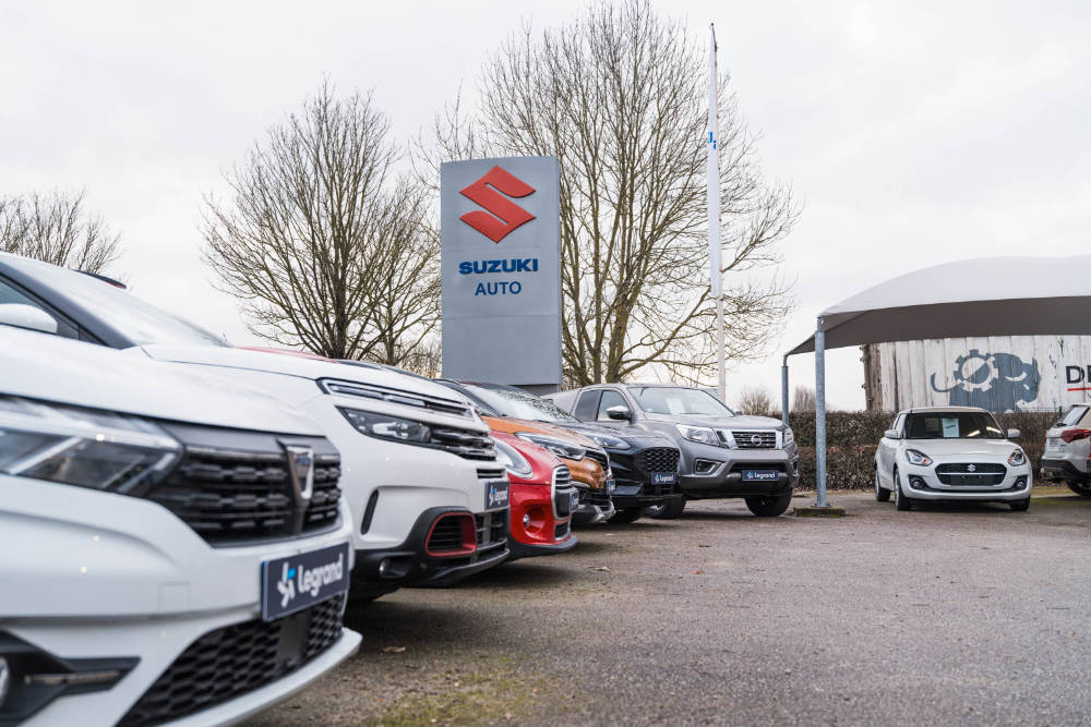 Park des véhicules avec en fond le totem de la marque Suzuki et la concession Ford Suzuki Pont-Audemer